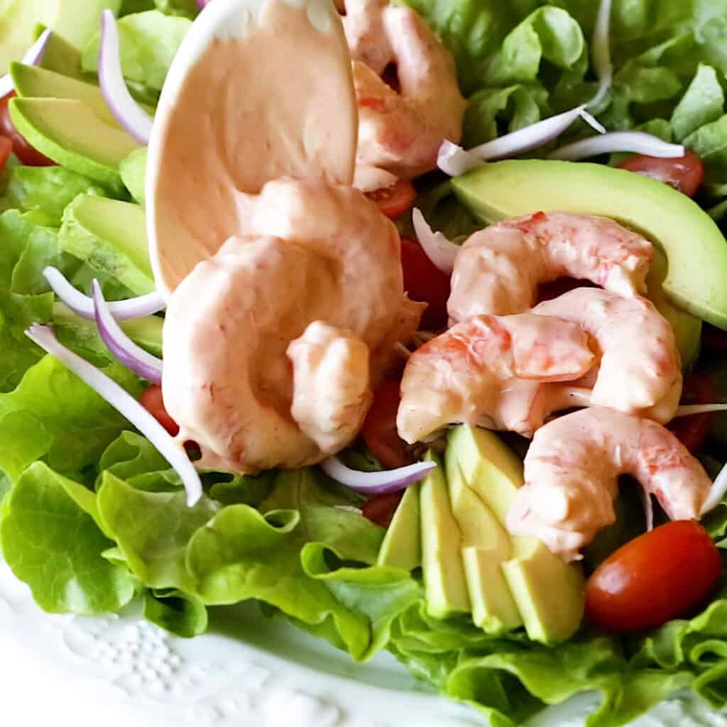 Adding spoonfuls of sauce covered prawns to the salad platter.