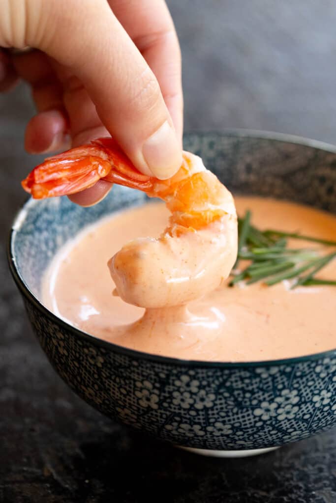 A shrimp is dipped into a bowl of Marie Rose sauce.