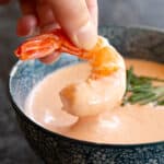 A prawn is dipped into a bowl of seafood sauce.