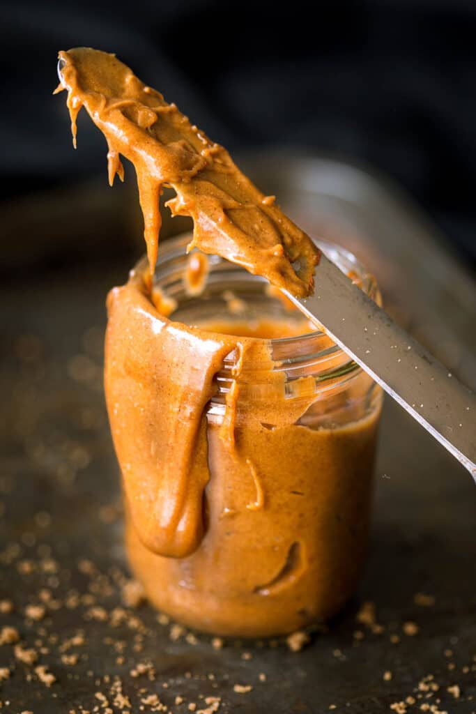 Speculoos cookie butter drips off a knife and down the side of a jar.