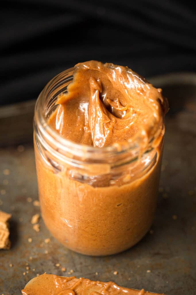 Spiced cookie butter in a jar with crumbs around it on a tray.