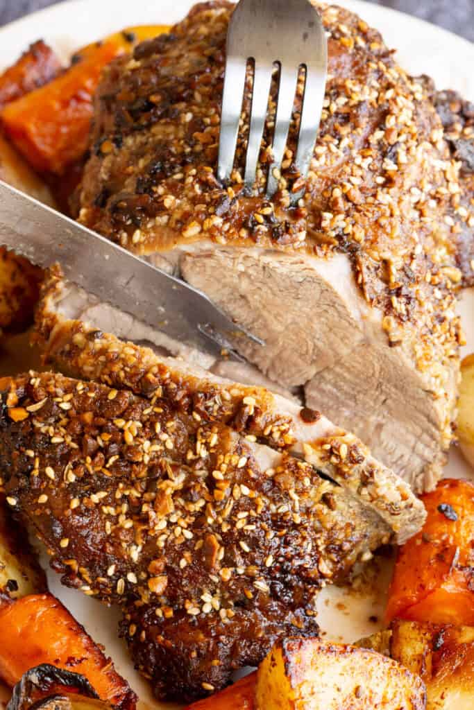 A knife carves through dukkah crusted rolled lamb roast.
