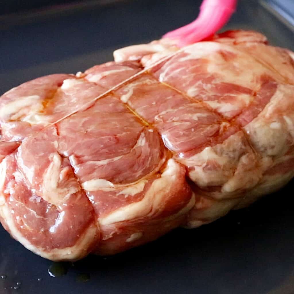 An brush bastes oil on a rolled lamb shoulder.