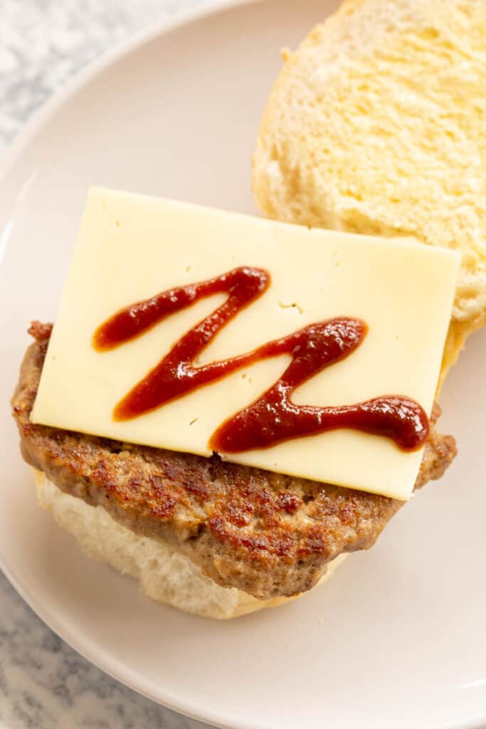 An open bread roll with a square sausage, cheese and brown sauce.