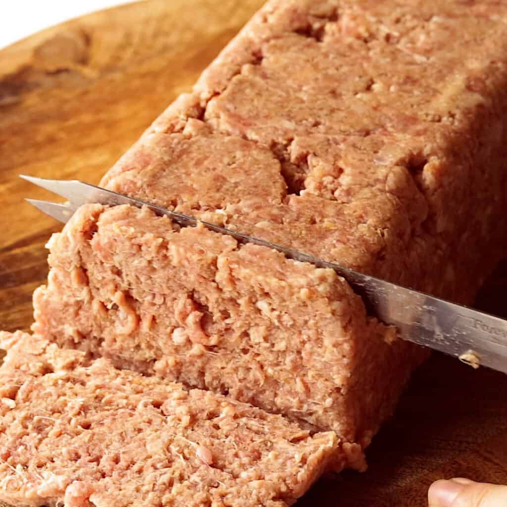 Cutting the square sausage loaf with a serrated knife.