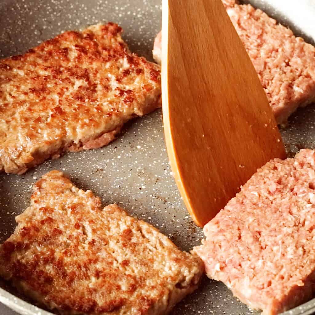 Frying square sausage slices in a large frying pan.