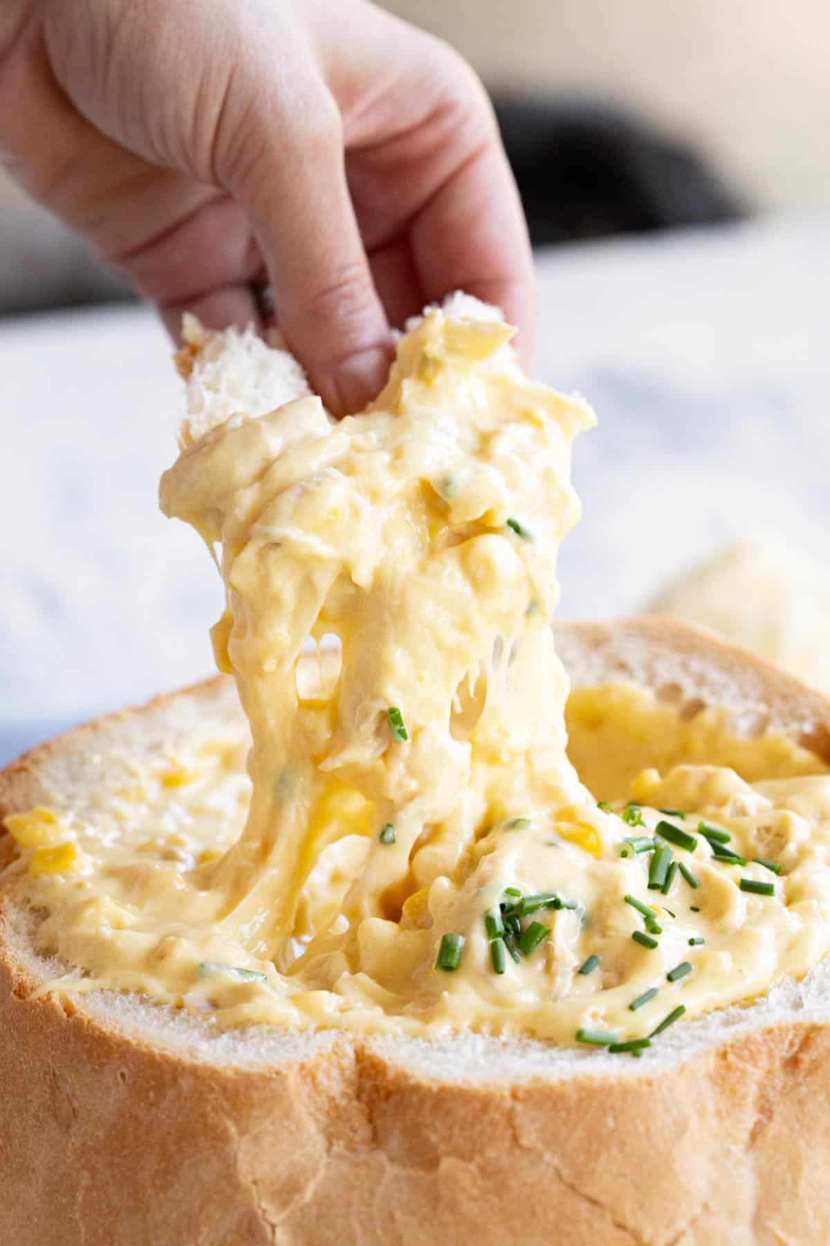 A hand lifts a piece of bread loaded with creamy chicken and corn dip.