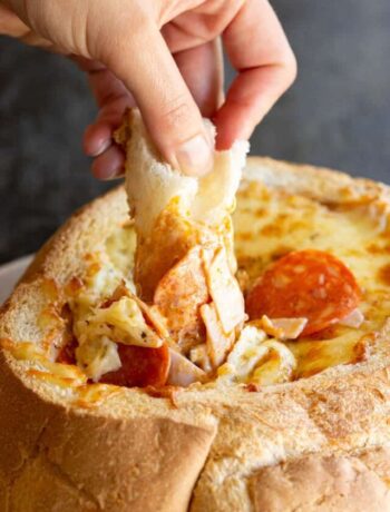 A hand dips a piece of bread into the pizza cob loaf dip.
