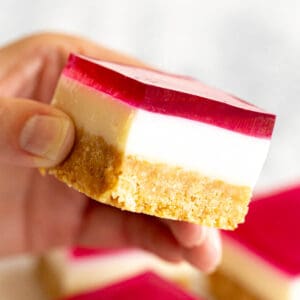 A hand holding a three layered jelly slice.