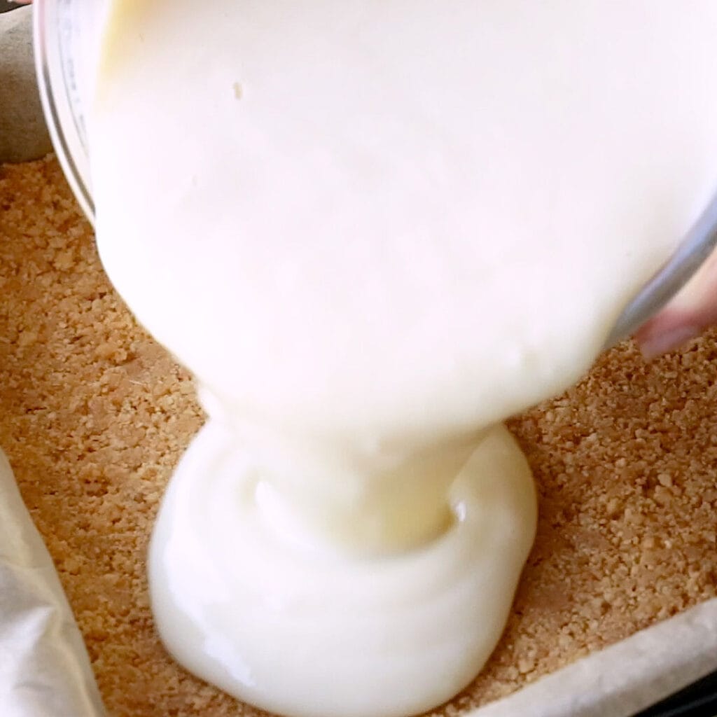 Pouring the condensed milk layer onto the biscuit base.