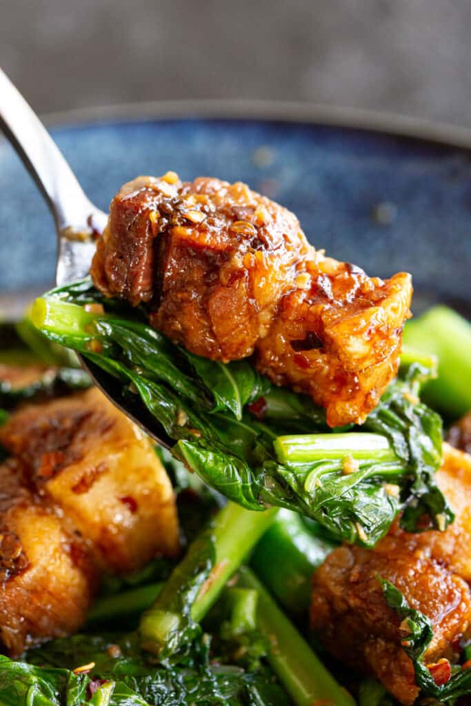 A piece of crispy pork belly with Chinese broccoli on a fork.