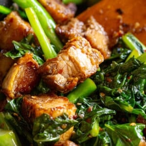 Crispy pieces of pork belly tossed with greens in a frying pan.