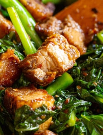 Crispy pieces of pork belly tossed with greens in a frying pan.