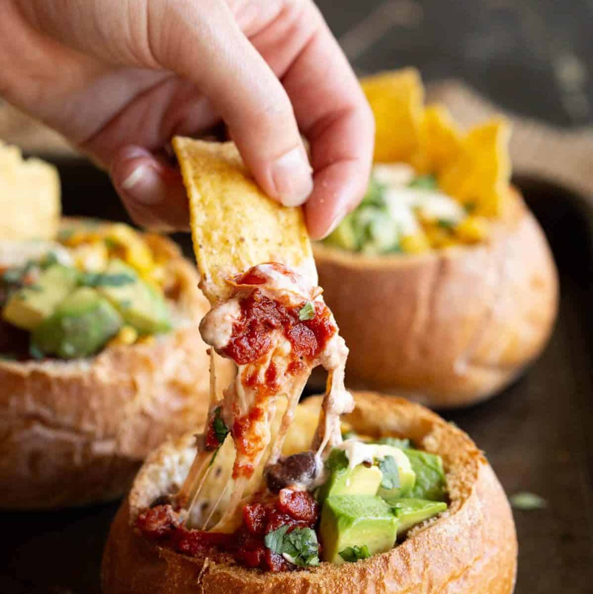 A tortilla chip dips into a mini Mexican bread bowl.