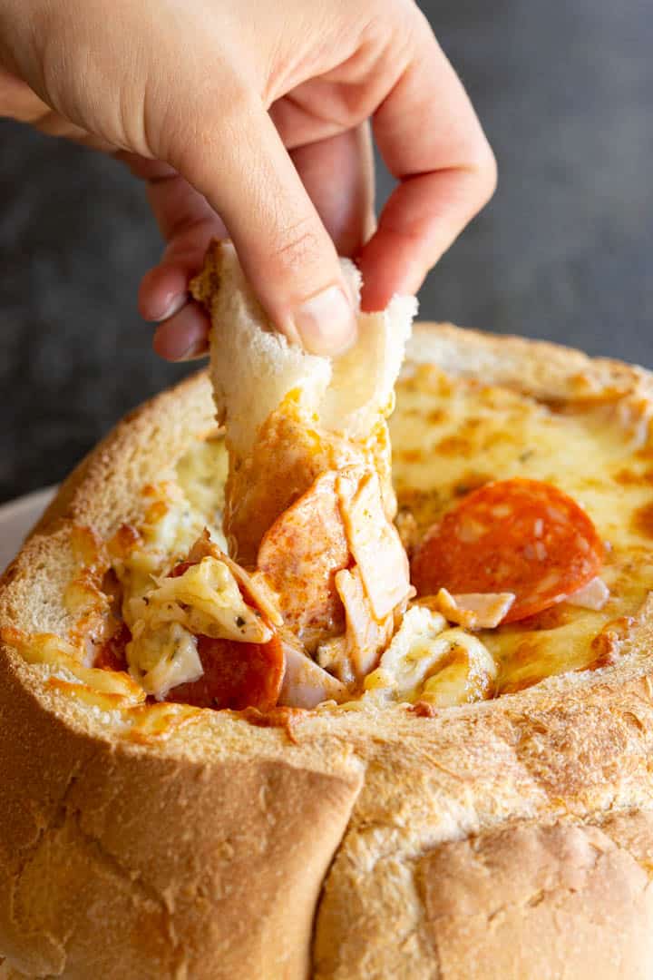 A hand dips a piece of bread into the pizza cob loaf dip.
