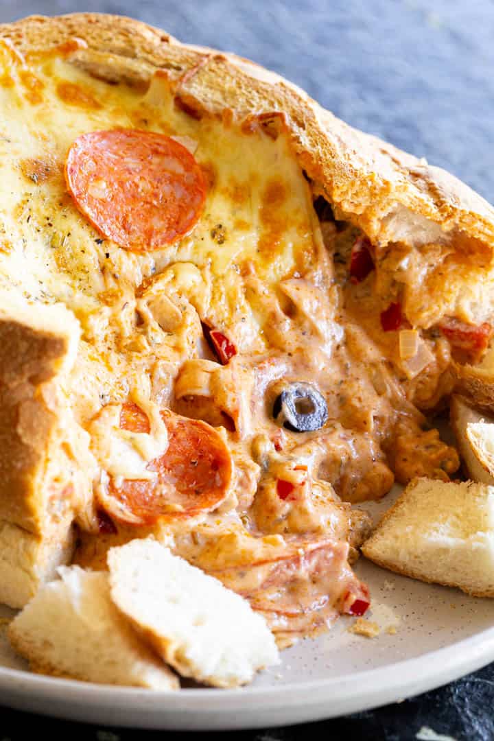 Creamy pizza dip oozes out of a cob loaf bread bowl.