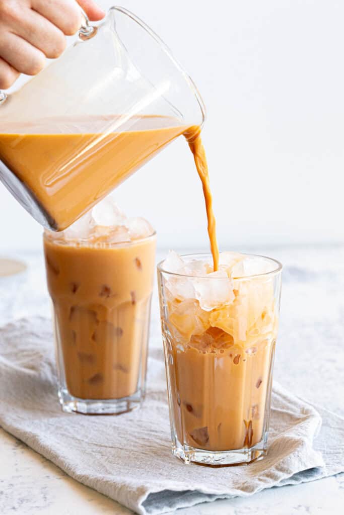 A jug pours orange Thai iced tea into a glass filled with ice.