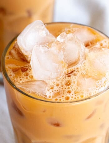 A frosty glass of Thai iced tea with ice cubes.