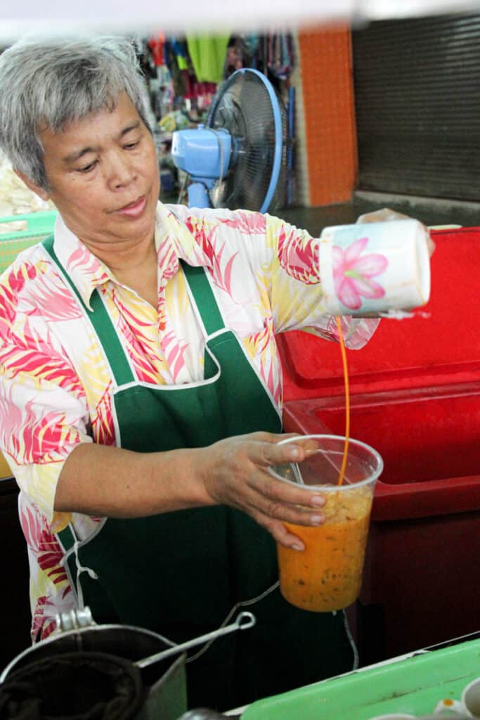 Lady pours Thai tea into large cup.