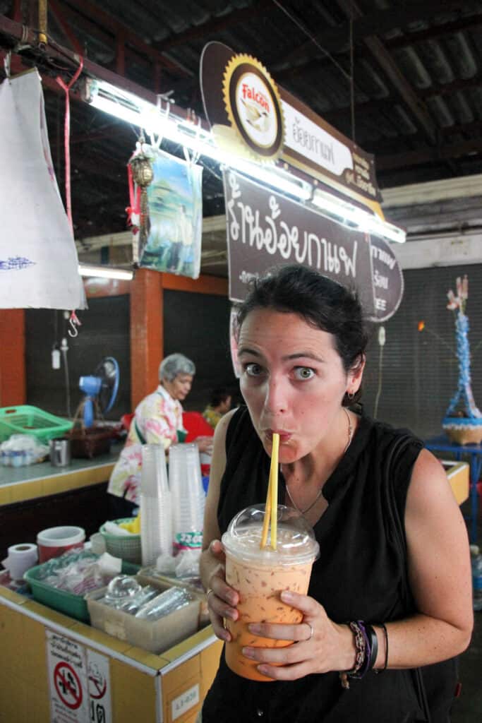 Woman sipping on large cup of Thai iced tea in Chiang Mai food market.