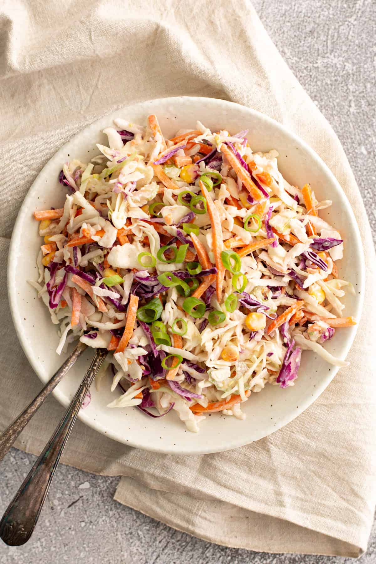A wide bowl filled with coleslaw and two salad servers.
