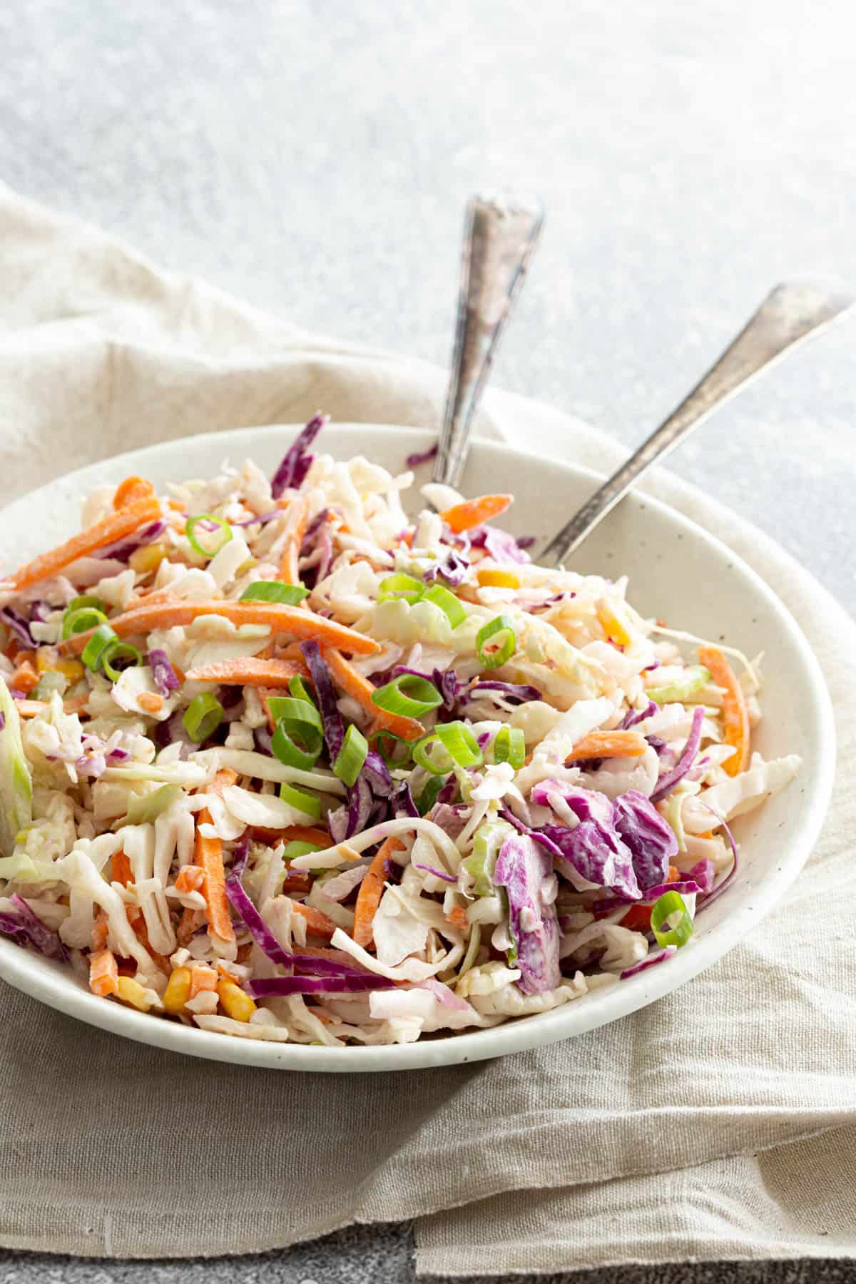 A white bowl filled with Japanese style coleslaw with silver salad servers.