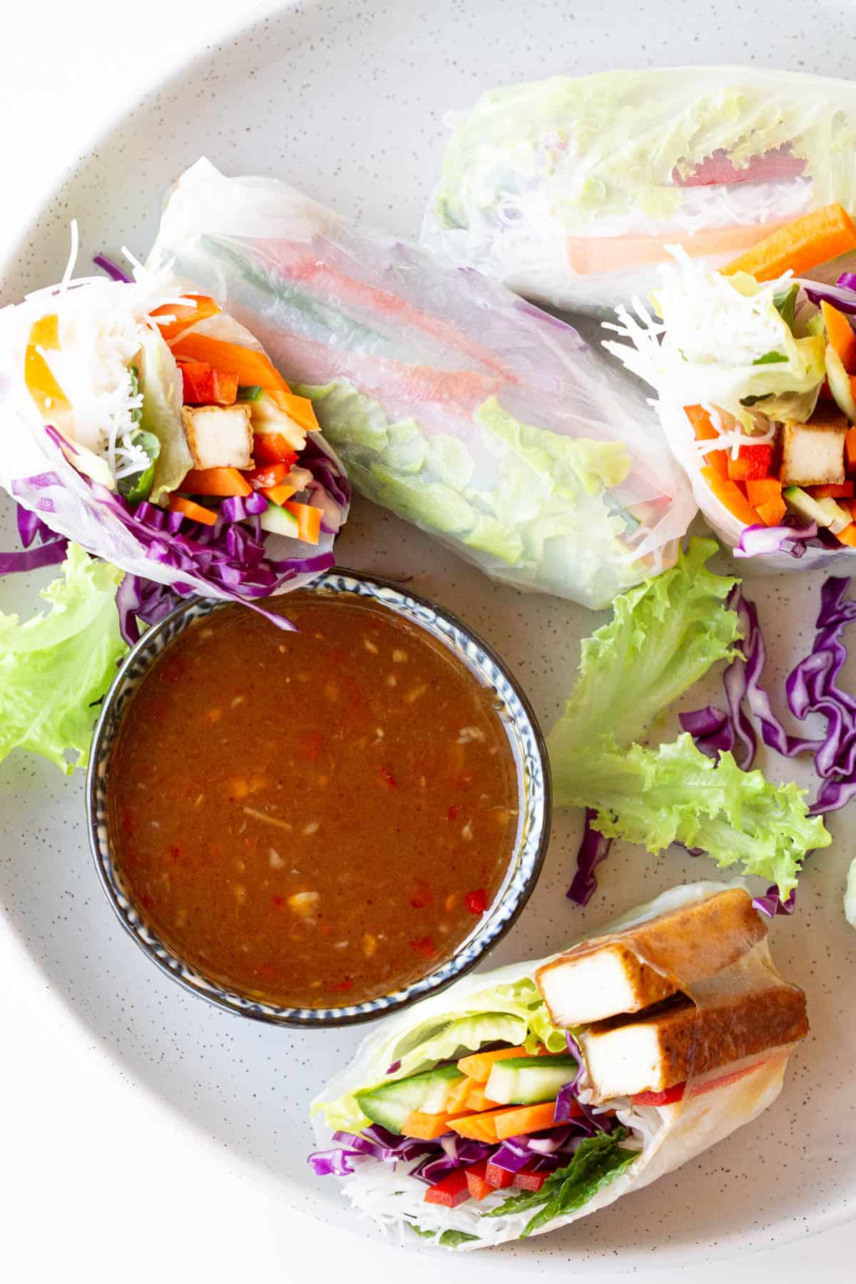 Rainbow rice paper rolls surround a dish of tamarind dipping sauce.