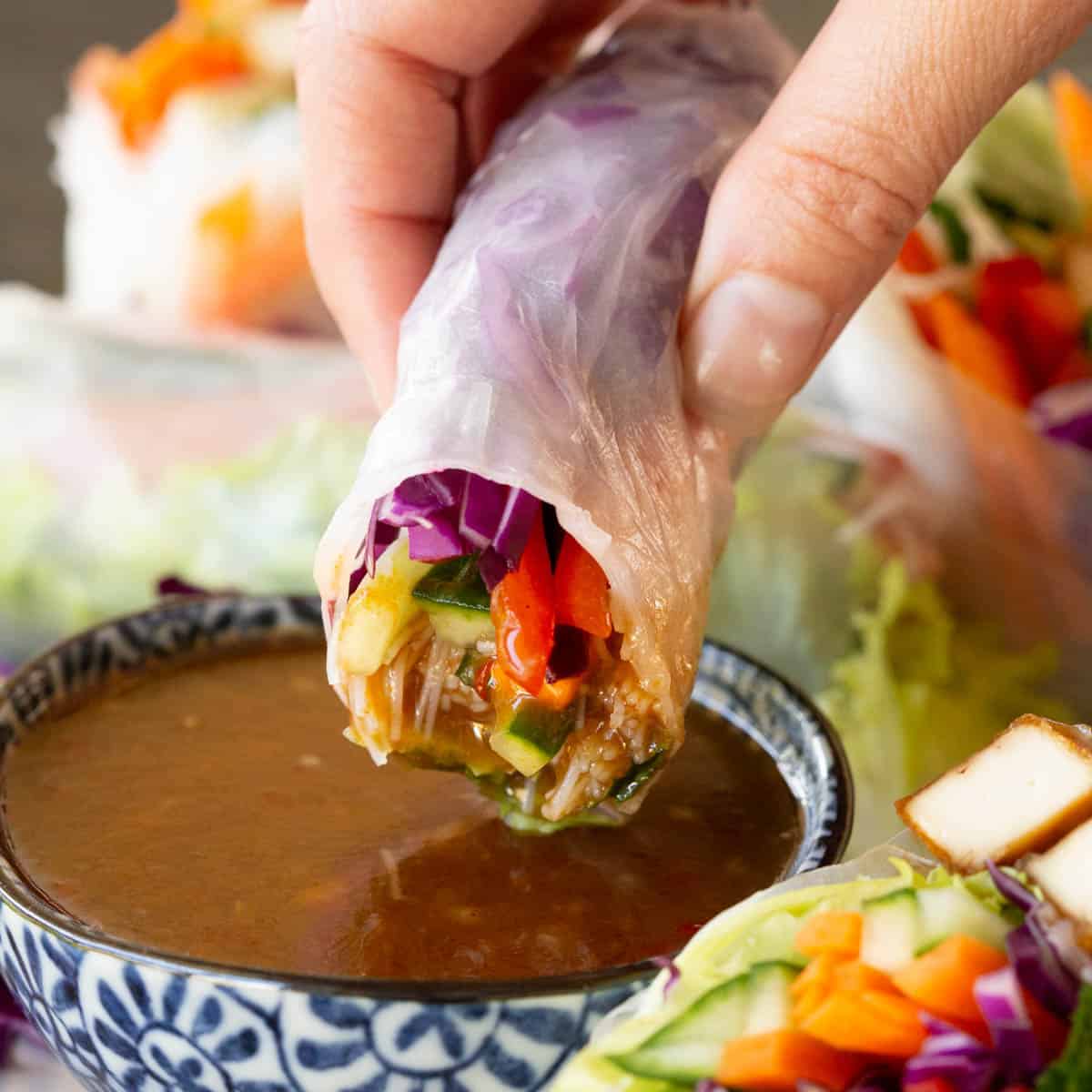 A hand dips a rice paper roll into tamarind sauce.