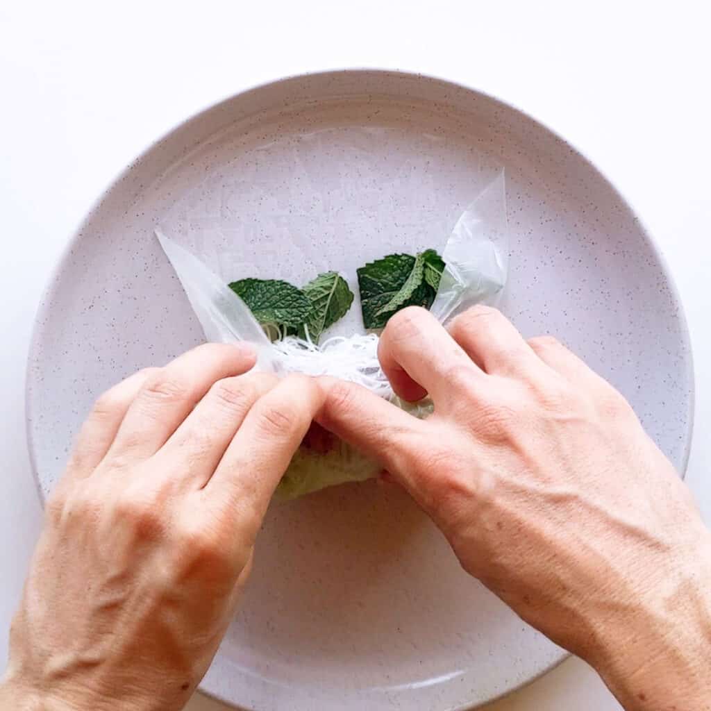 Rolling the rice paper wrapper over the mint.