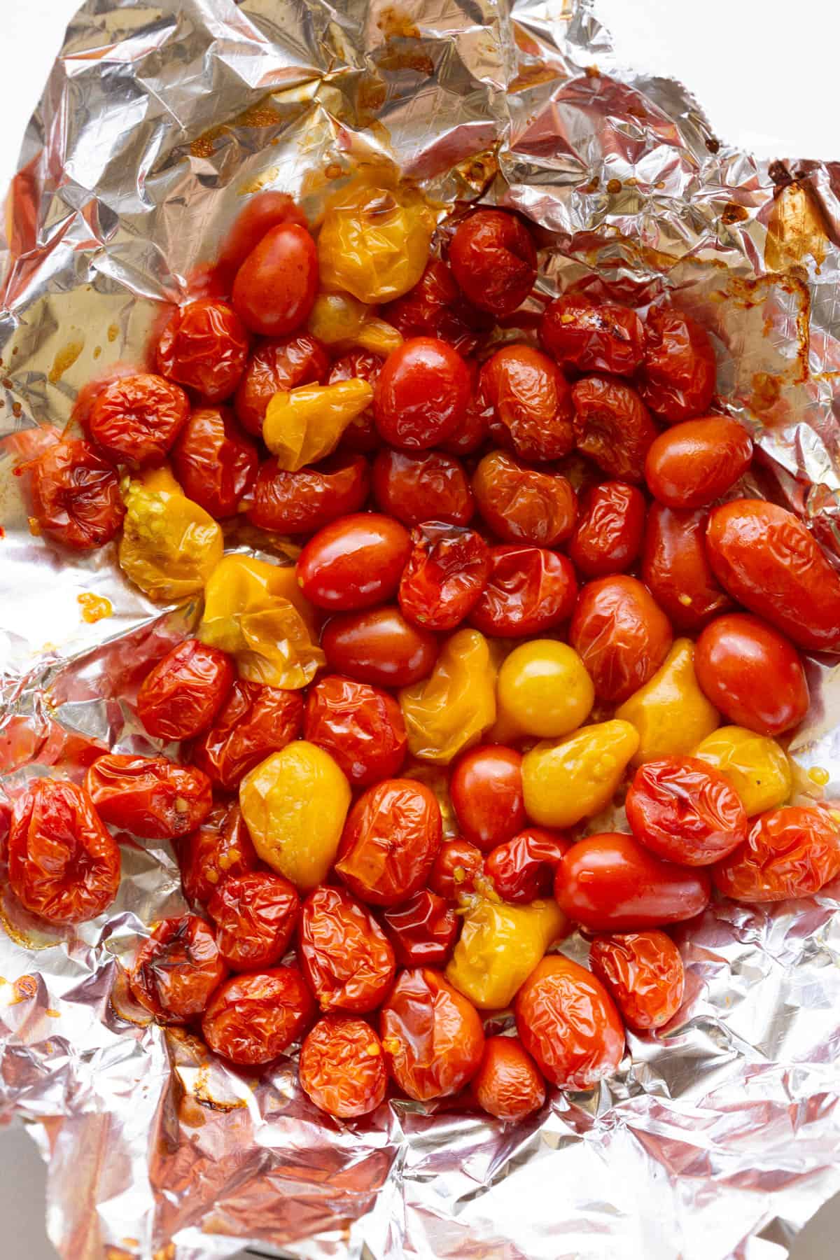 A sheet of aluminium foil layered with yellow and red roasted cherry tomatoes.