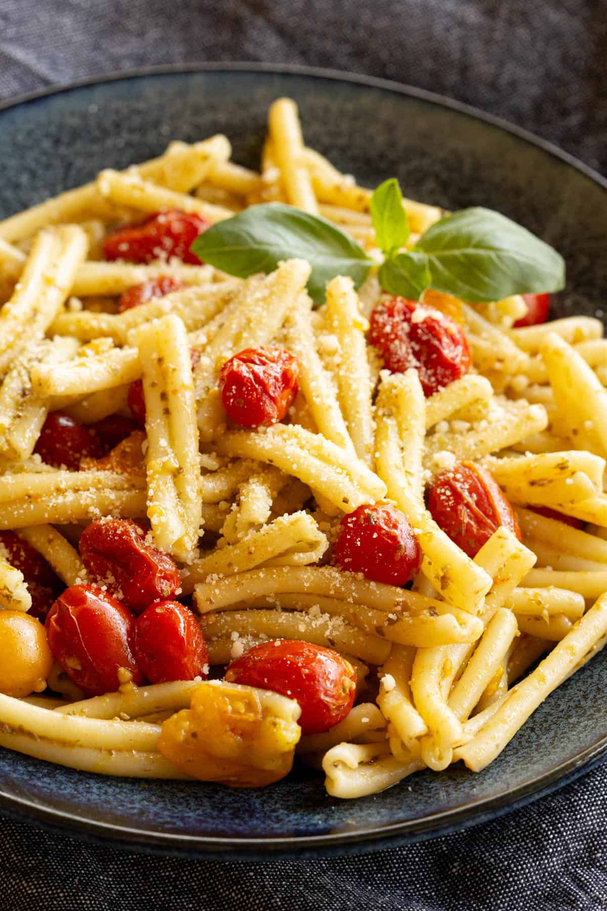 A blue bowl filled with golden pasta, bursts of red cherry tomato and a hint of green basil.