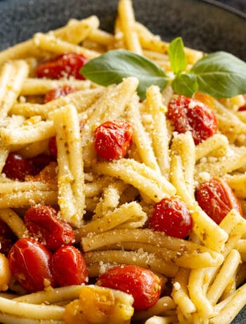 A bowl of cherry tomato pesto pasta topped with Parmesan cheese and fresh basil.