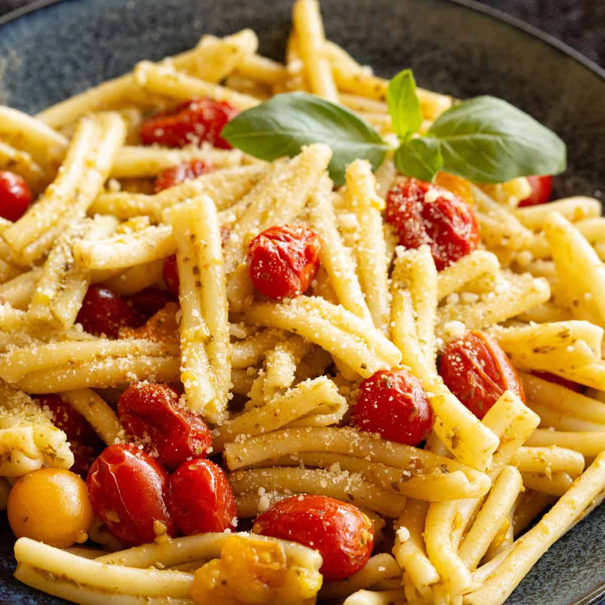 A bowl of cherry tomato pesto pasta topped with Parmesan cheese and fresh basil.