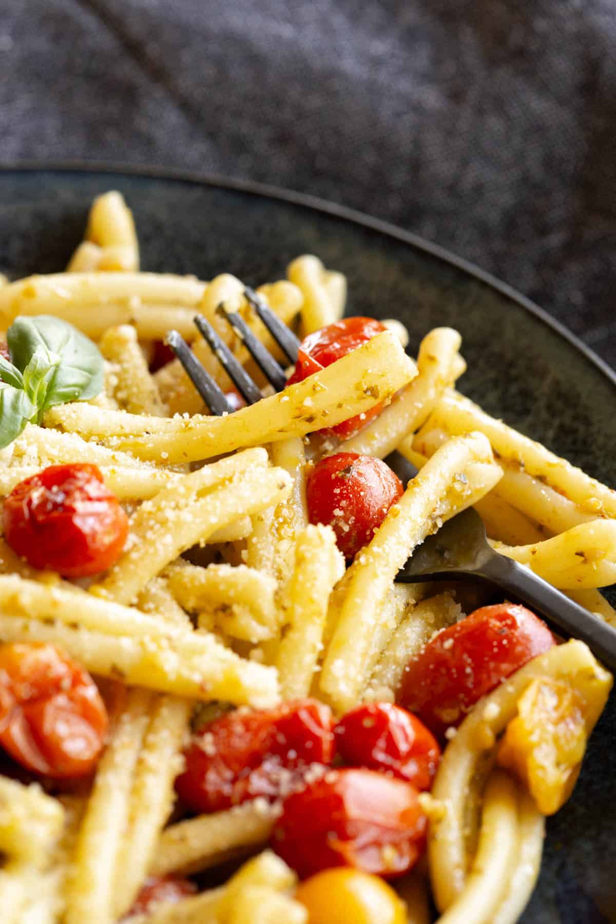 A black fork sits in a bowl filled with cherry tomato pesto pasta.