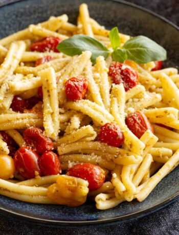 A blue bowl filled with golden pasta, bursts of red cherry tomato and a hint of green basil.