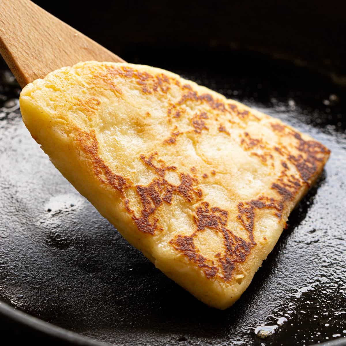 A spatula flips a tattie scone on a cast iron frying pan.
