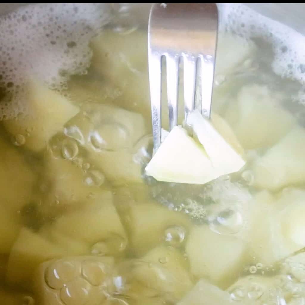 A fork pierces a mash potato to check it's cooked through.