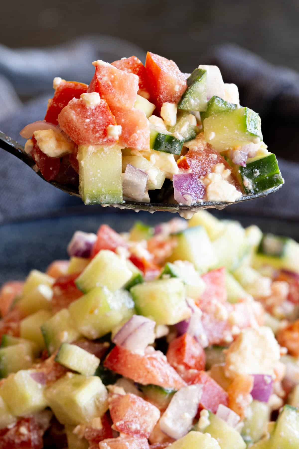 A spoon holds a combination of chopped onion, tomato, cucumber and feta.