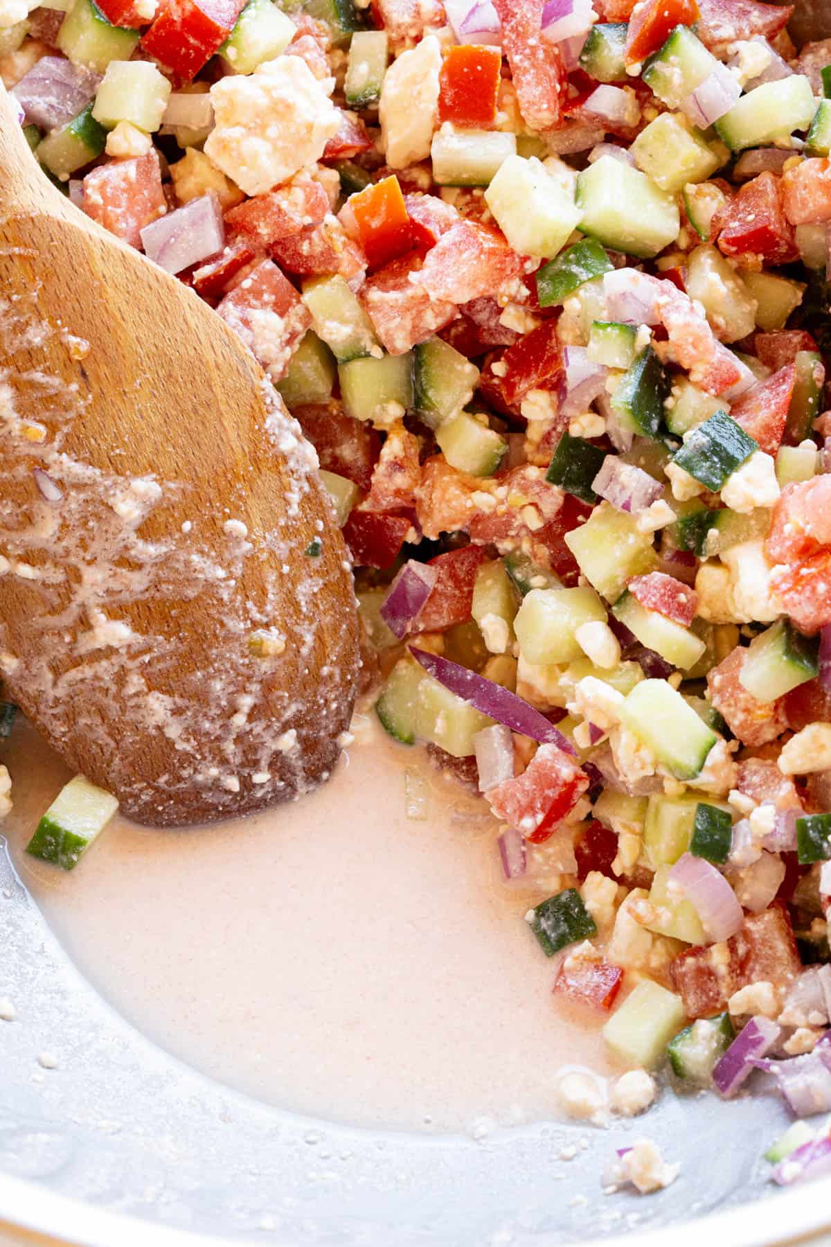 A wooden spoon pulls back chopped salad to show the self made sauce at the bottom.
