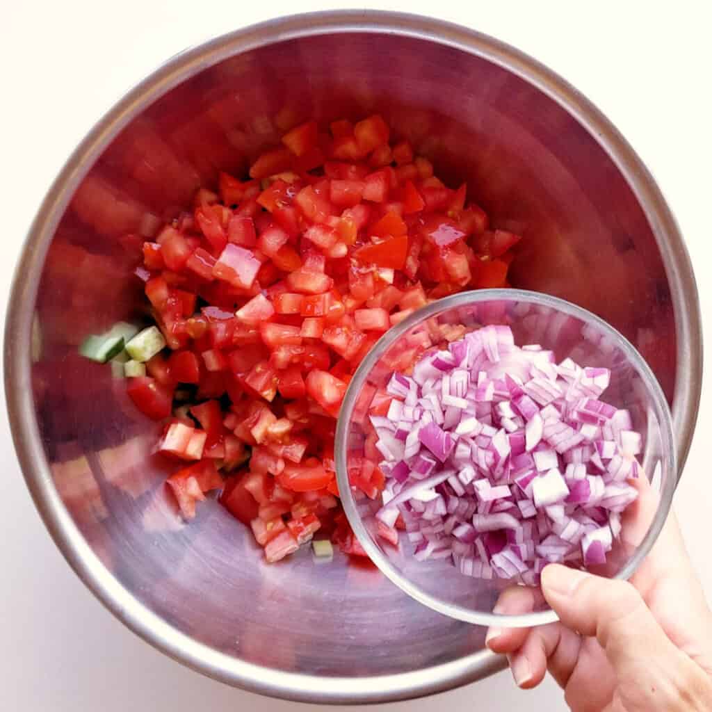 A small bowl of red onion is poured into a big salad bowl.