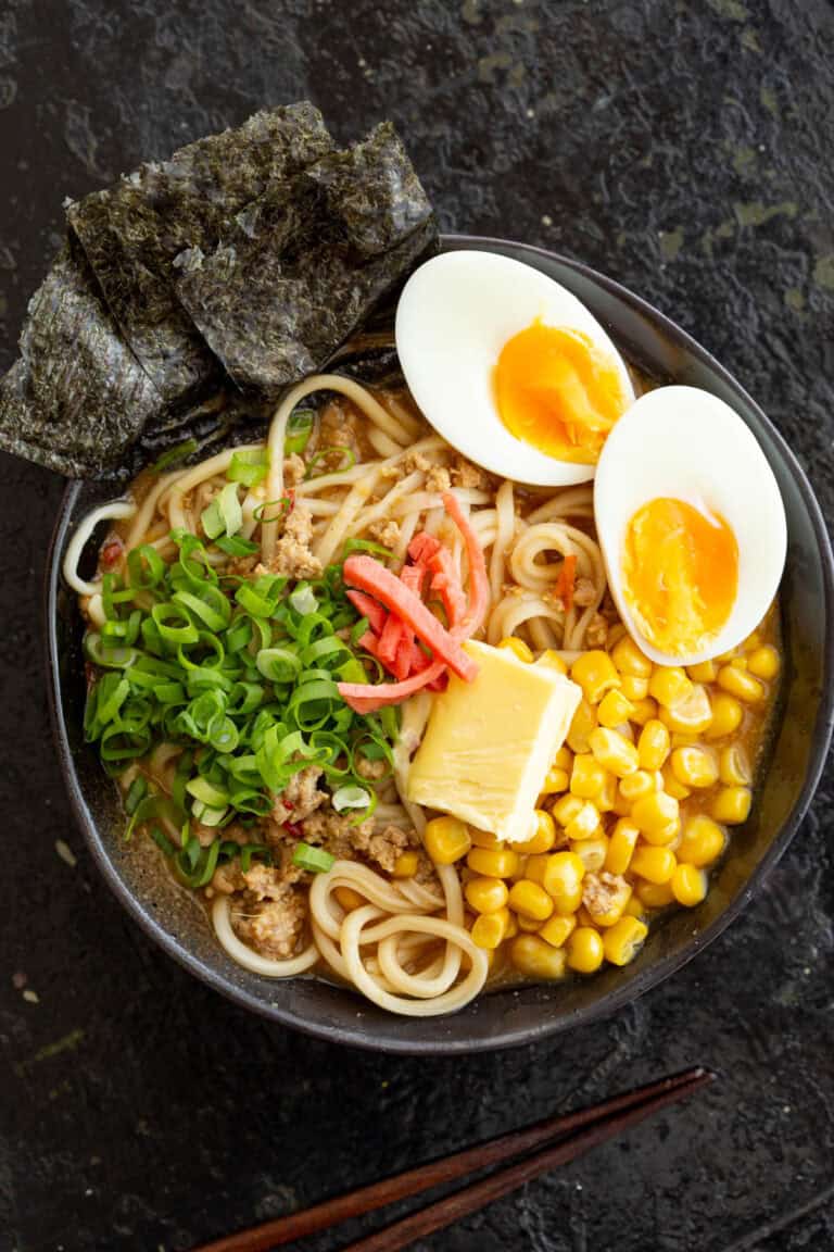 A bowl of miso ramen topped with ajitama eggs, corn, butter and spring onion.
