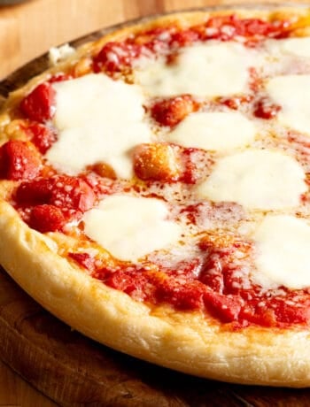 A pizza topped with tomato sauce and bocconcini on a wooden board.