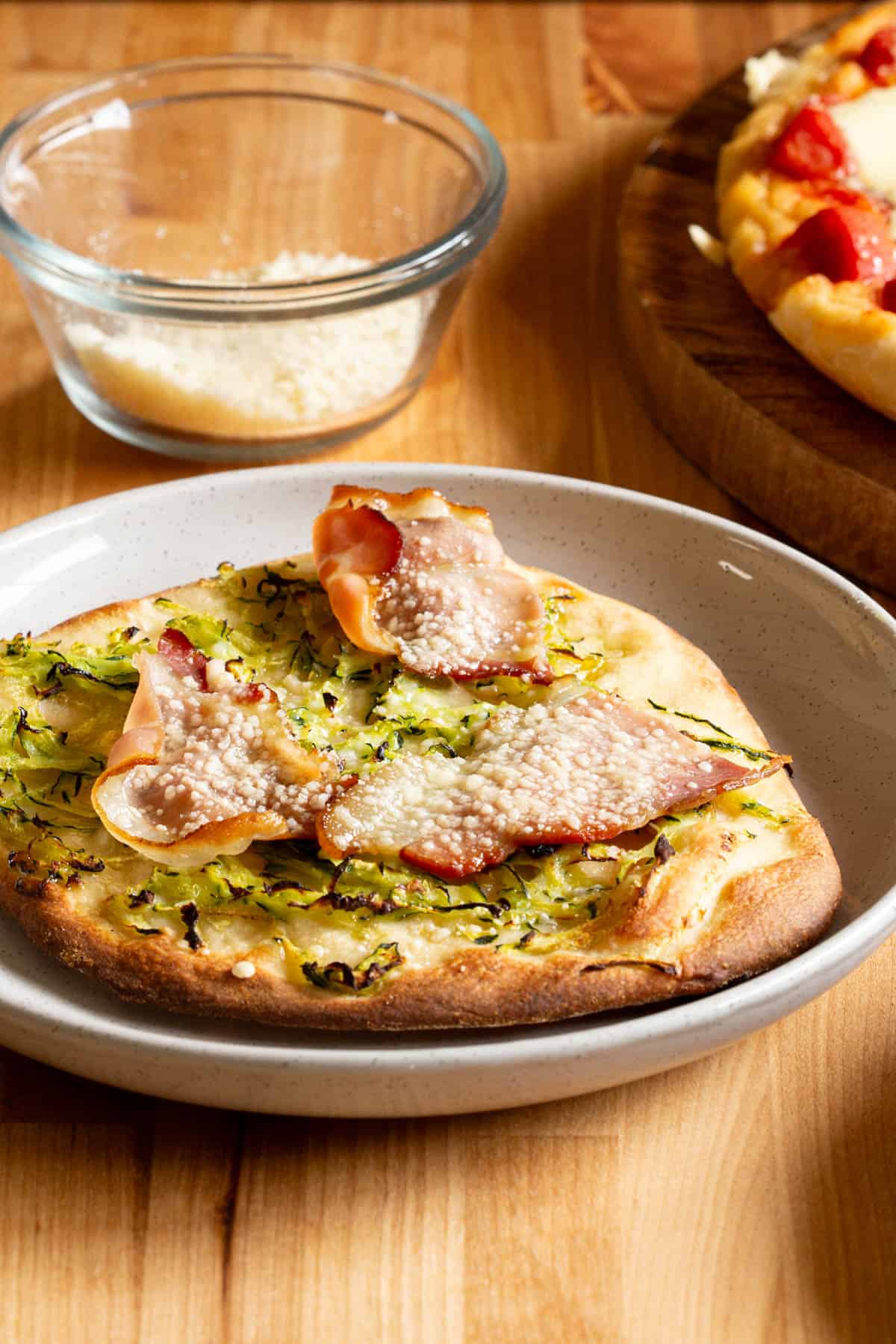 A small pizza with a prosciutto, Parmesan and zucchini topping.
