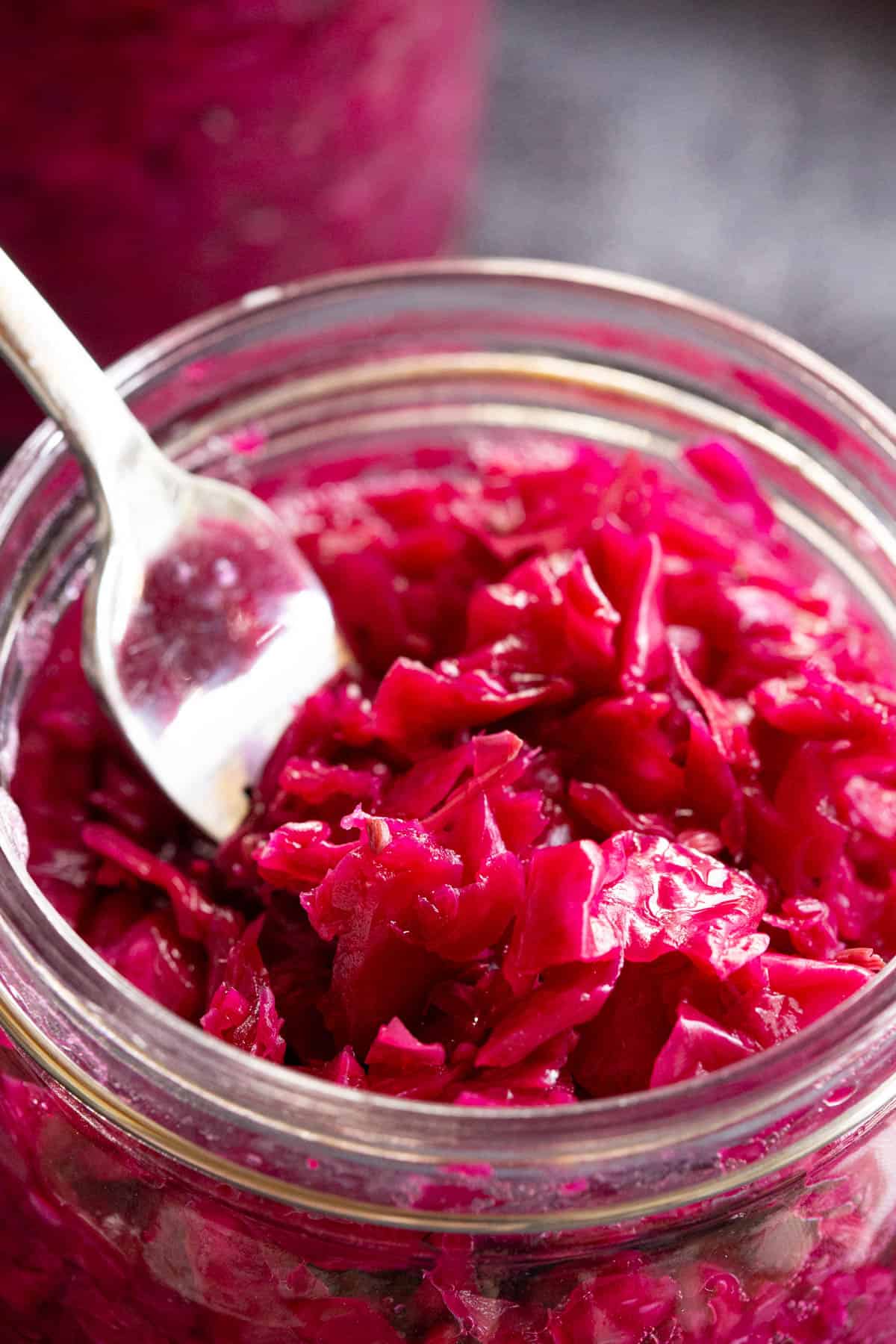 A fork scoops out bright red sauerkraut from a jar.