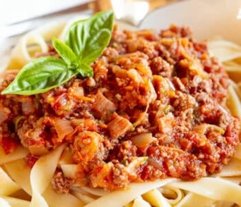 A bowl of Bolognese pasta garnished with fresh basil.