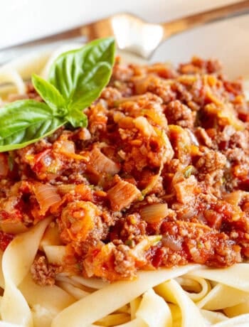 A bowl of Bolognese pasta garnished with fresh basil.