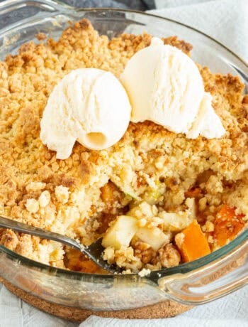 A persimmon crumble pie showing the chunks of apple and persimmon with ice cream.