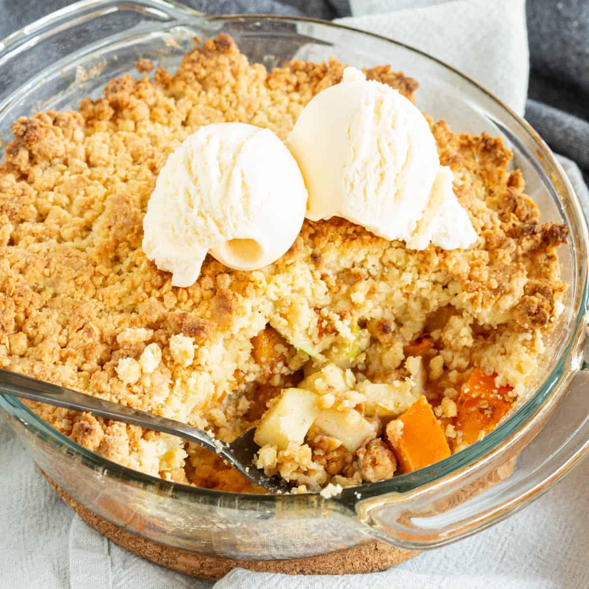 A persimmon crumble pie showing the chunks of apple and persimmon with ice cream.